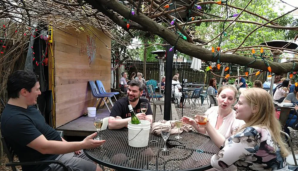 A group of friends is enjoying drinks and conversation at an outdoor patio decorated with colorful lights