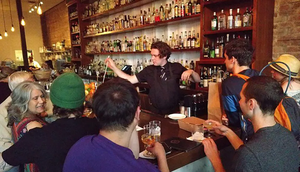 A group of people enjoy each others company at a bar bustling with activity and a bartender in the process of serving drinks