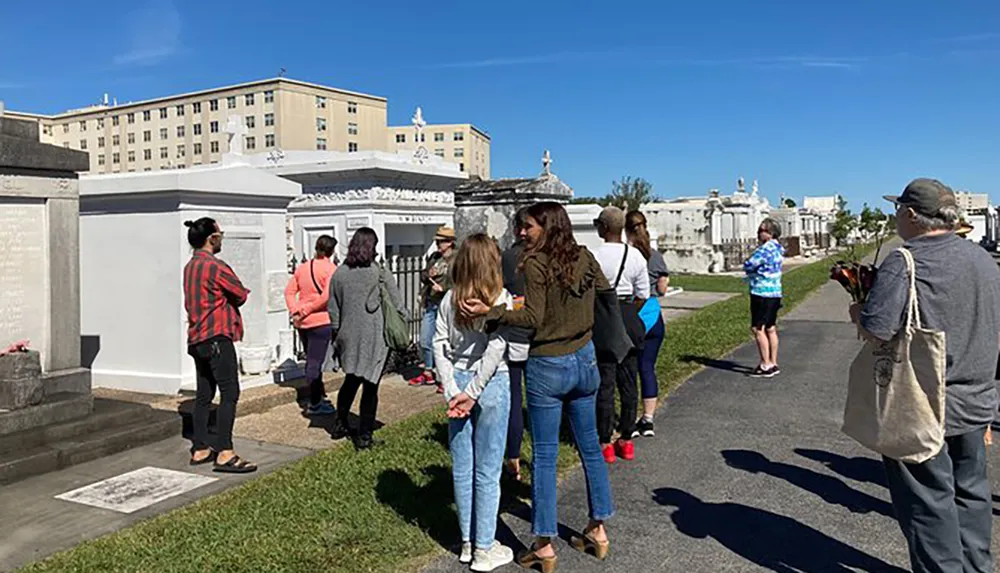 A group of people is taking a tour around a cemetery with above-ground tombs under a clear blue sky