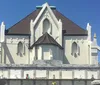 The image shows an ornate entrance gate to Saint Roch Campo Santo cemetery with statues on either side and a sunlit path leading into the burial grounds