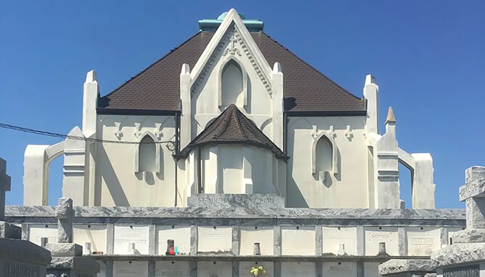 This image shows a distinctive white building that appears to be a mausoleum featuring Gothic architectural elements and situated under a clear blue sky