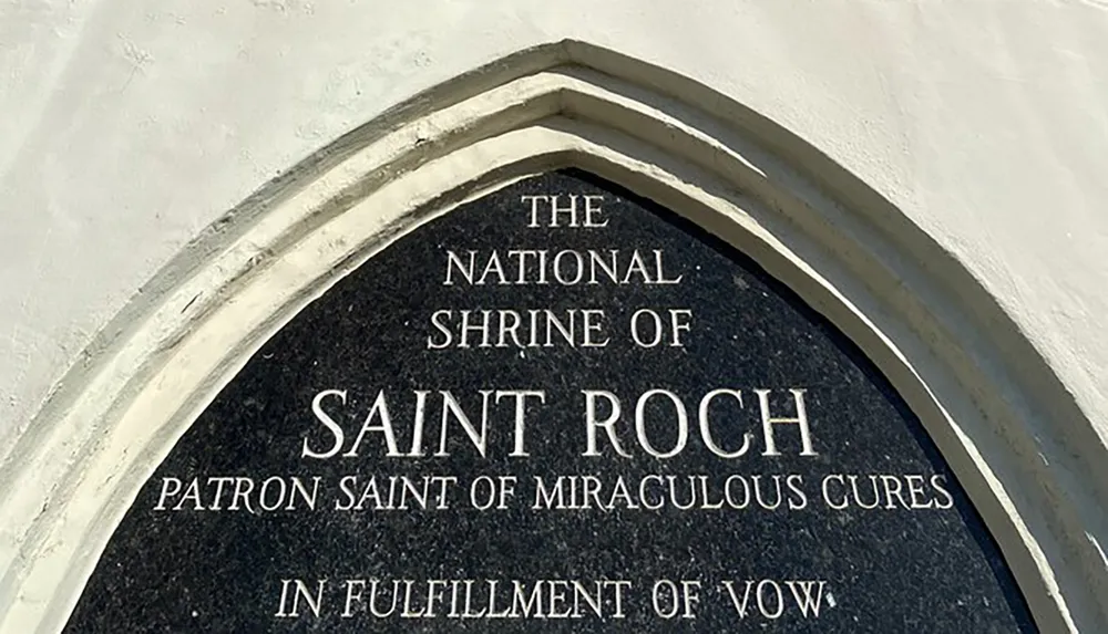 The image shows an arched sign that reads The National Shrine of Saint Roch Patron Saint of Miraculous Cures In Fulfilment of Vow