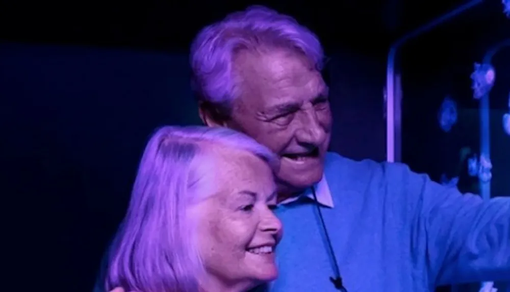 A smiling older couple is taking a selfie together backlit by a blue light that gives a calming hue to the scene