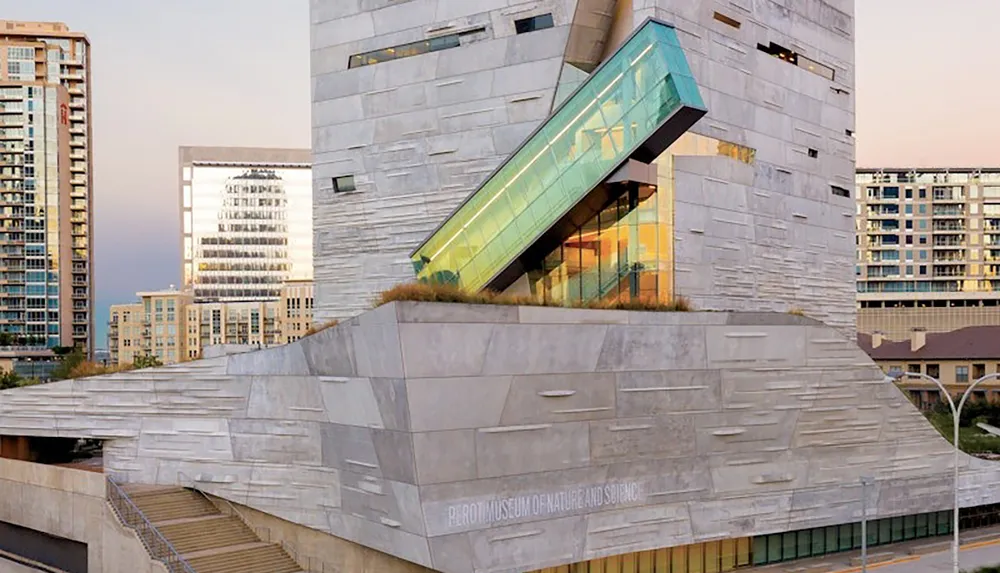 The image shows the modern and angular architecture of the Perot Museum of Nature and Science set against an urban background at dusk