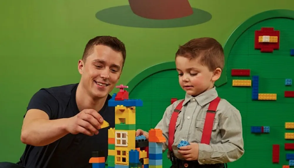 A man and a young child are happily engaged in building a colorful structure out of LEGO bricks in a play area