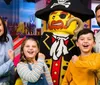 A family is posing with a life-sized Lego pirate figure all smiling cheerfully in a colorful playful setting