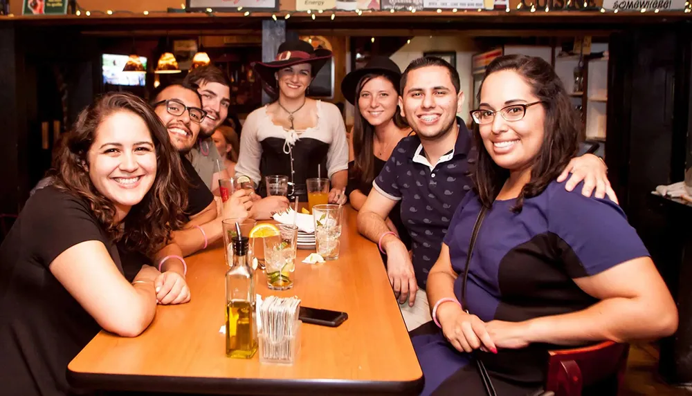 A group of seven people is smiling at the camera in a friendly gathering at a bar or restaurant