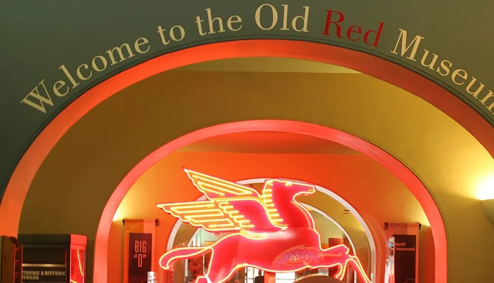 The image features a warm-lit archway entrance with the words Welcome to the Old Red Museum displayed above and a neon-lit Pegasus logo in the center