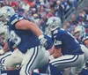 Players in football uniforms are poised for action during a game with a focus on the offensive line and quarterback preparing for the next play