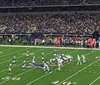 Players in football uniforms are poised for action during a game with a focus on the offensive line and quarterback preparing for the next play