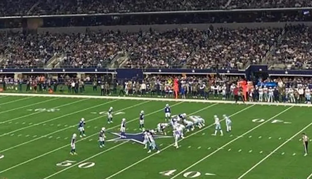 The image shows a football game in progress with players lined up for a snap in a stadium filled with spectators