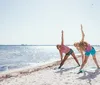 Two people are practicing a yoga pose on the beach on a sunny day