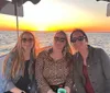 Three friends are enjoying a boat ride with a beautiful sunset over the water in the background