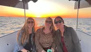 Three friends are enjoying a boat ride with a beautiful sunset over the water in the background.