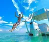 A person is jumping off the back of a pontoon boat into clear blue waters under a sunny sky
