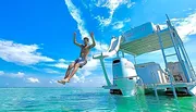 A person is jumping off the back of a pontoon boat into clear blue waters under a sunny sky.