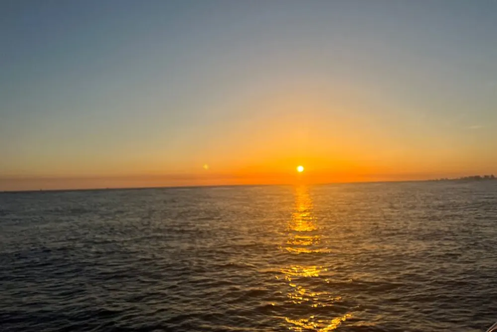 The image shows a serene sunset over the ocean with the sun casting a golden reflection on the water