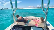Two adults and a child are relaxing on a boat with clear turquoise waters in the background.