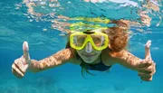 A person is giving two thumbs up while snorkeling underwater, wearing a yellow mask.