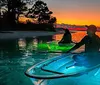 Two individuals are kayaking on clear luminous waters against a stunning sunset backdrop