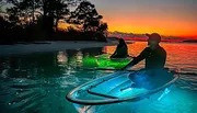 Two individuals are kayaking on clear, luminous waters against a stunning sunset backdrop.