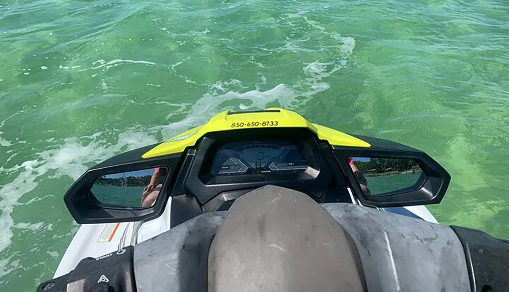 The image shows a first-person view from a jet ski rider cruising over green-tinted water with the dashboard and handlebars of the jet ski visible in the foreground