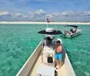 A man gives a thumbs-up while happily displaying a small fish in front of a boat anchored in shallow waters