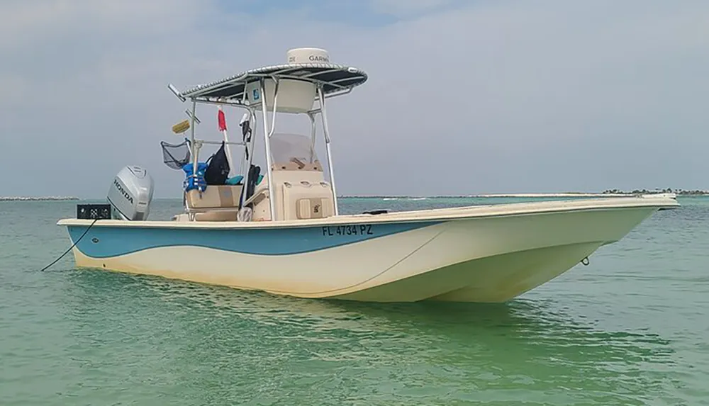 A center console boat is anchored in shallow clear waters near a sandbar