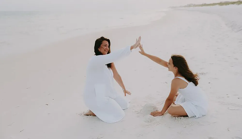 Two people are on a beach giving each other a high-five with the water and horizon in the background