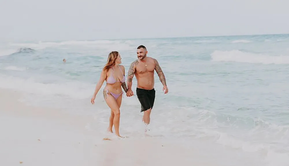 A couple is walking hand in hand along the shoreline on a beach smiling and enjoying each others company