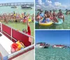 A group of people is joyfully posing for a selfie on a boat while another crowd in the water behind them is also partaking in the photo all set against a backdrop of a sunny busy waterway filled with boats