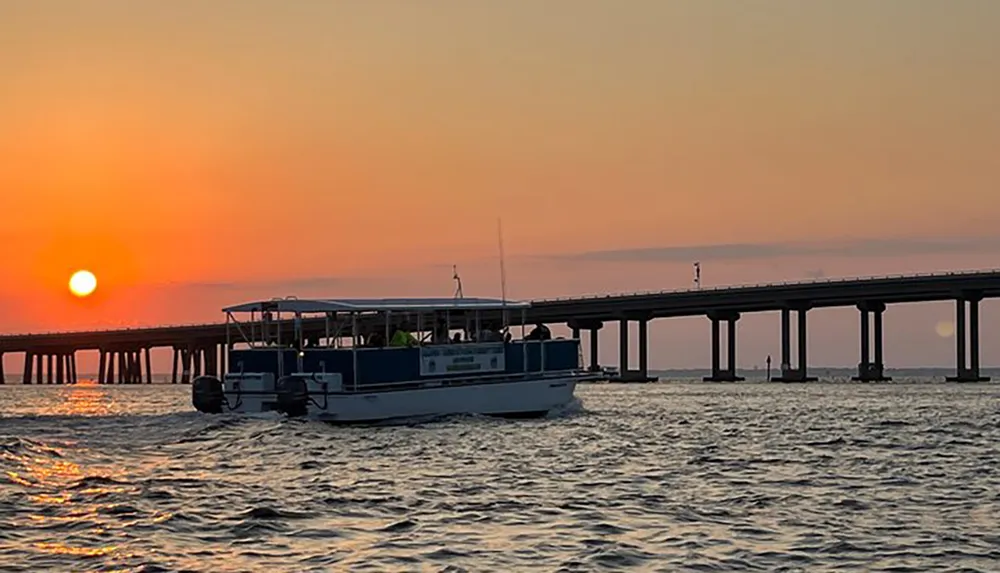 A boat glides on the water near a bridge under a sunset sky