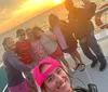 A group of five people are smiling and posing together on a boat with a beautiful sunset in the background