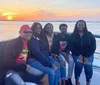 A group of five people are smiling and posing together on a boat with a beautiful sunset in the background