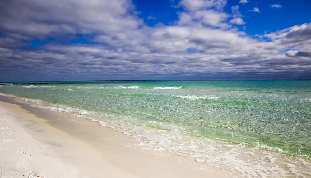 A serene beach scene with clear turquoise waters white sands and a sky partially covered with clouds