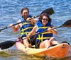 Two people are joyfully kayaking together on a sunny day both wearing life jackets and wielding paddles