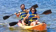 Two people are joyfully kayaking together on a sunny day, both wearing life jackets and wielding paddles.