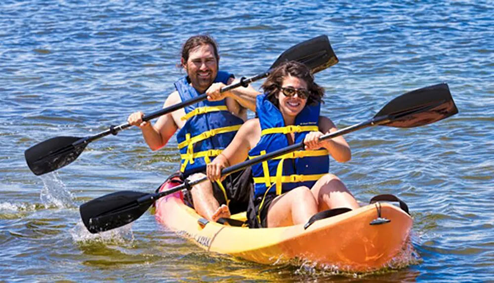 Two people are joyfully kayaking together on a sunny day both wearing life jackets and wielding paddles