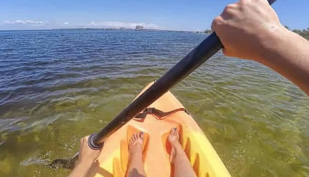 A persons point-of-view photograph while kayaking on a calm body of water with a paddle in hand and the front of the kayak visible