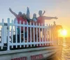 A group of smiling people in red shirts are posing behind a white fence on a boat at sunset