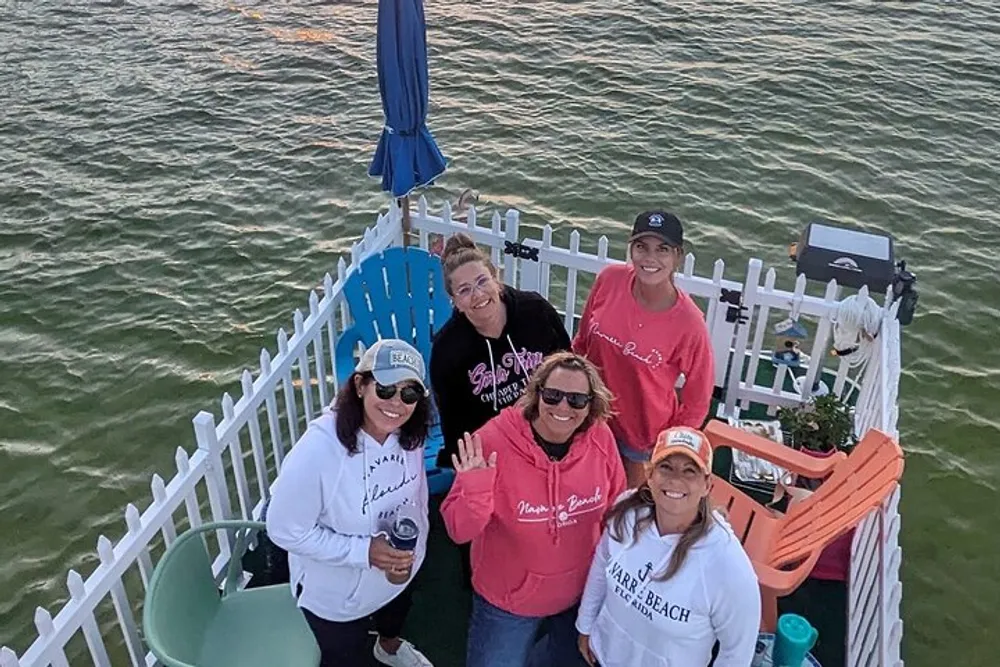 A group of five individuals is posing for a photo on a deck by the water during dusk exhibiting cheerful expressions