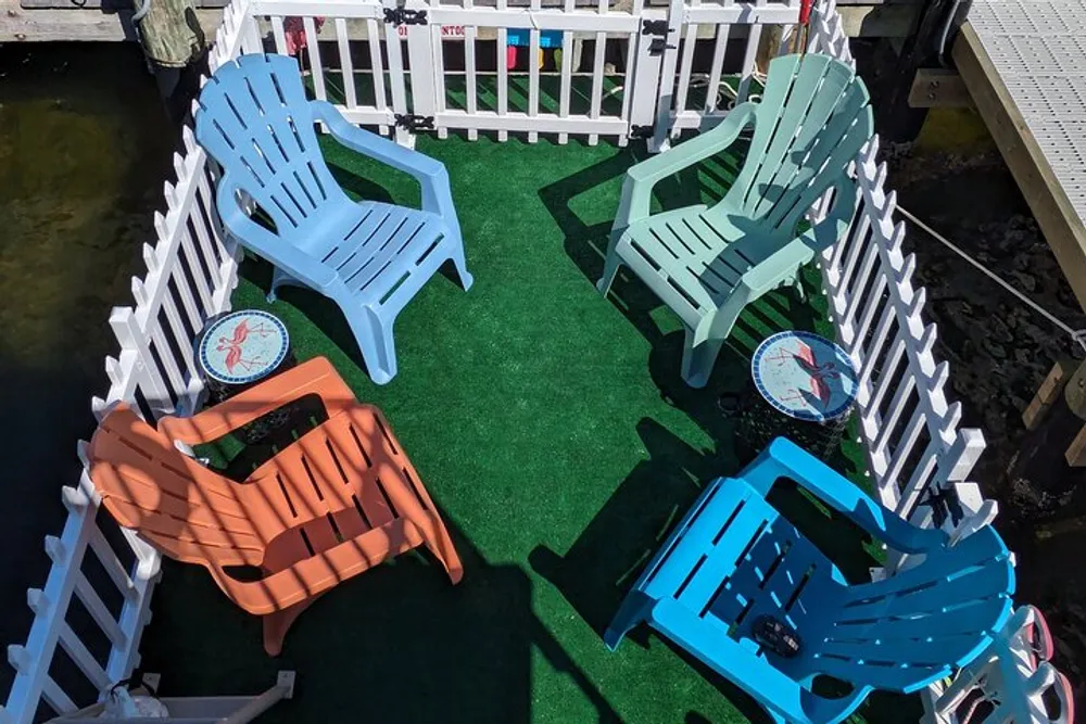 A colorful array of plastic chairs is arranged on a small artificial grass-floored and white-fenced patio creating a casual outdoor seating area