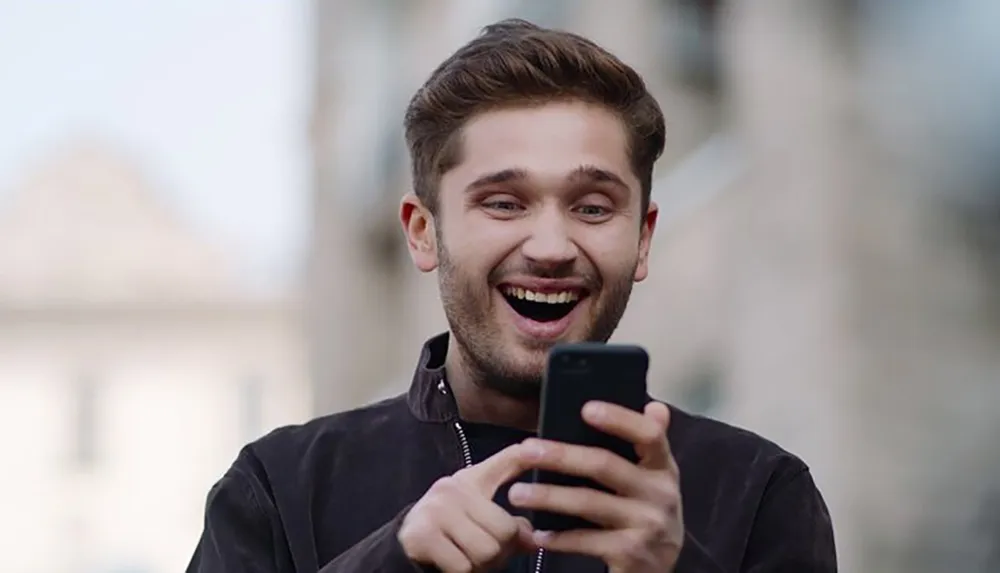 A young man laughs joyfully as he looks at his smartphone