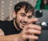 A group of cheerful young adults is taking a selfie with one of them holding the camera out in front capturing their smiling faces