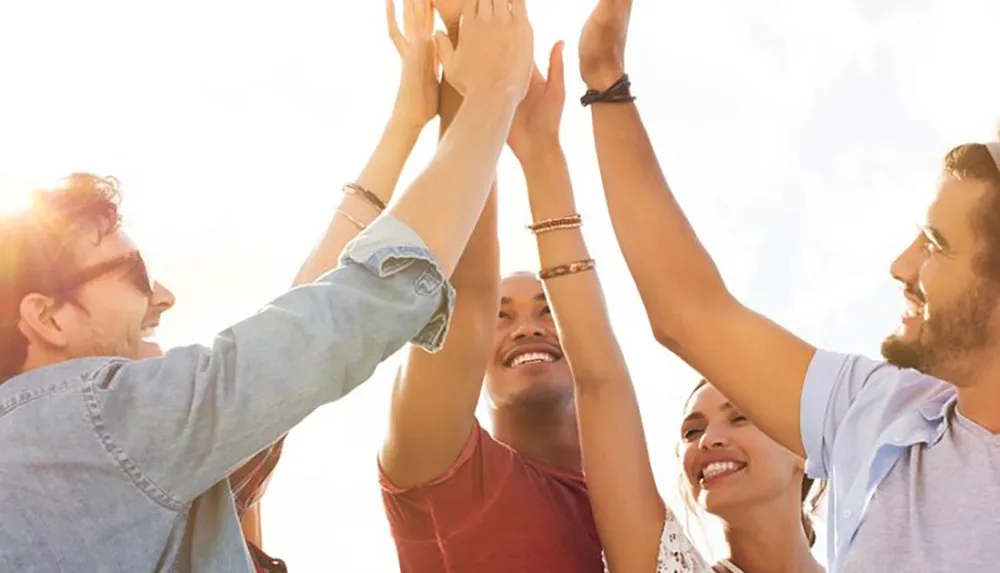 A group of joyful people participate in a teamwork hand stack under a bright sky symbolizing collaboration and unity