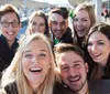 A group of cheerful young adults is taking a selfie with one of them holding the camera out in front capturing their smiling faces