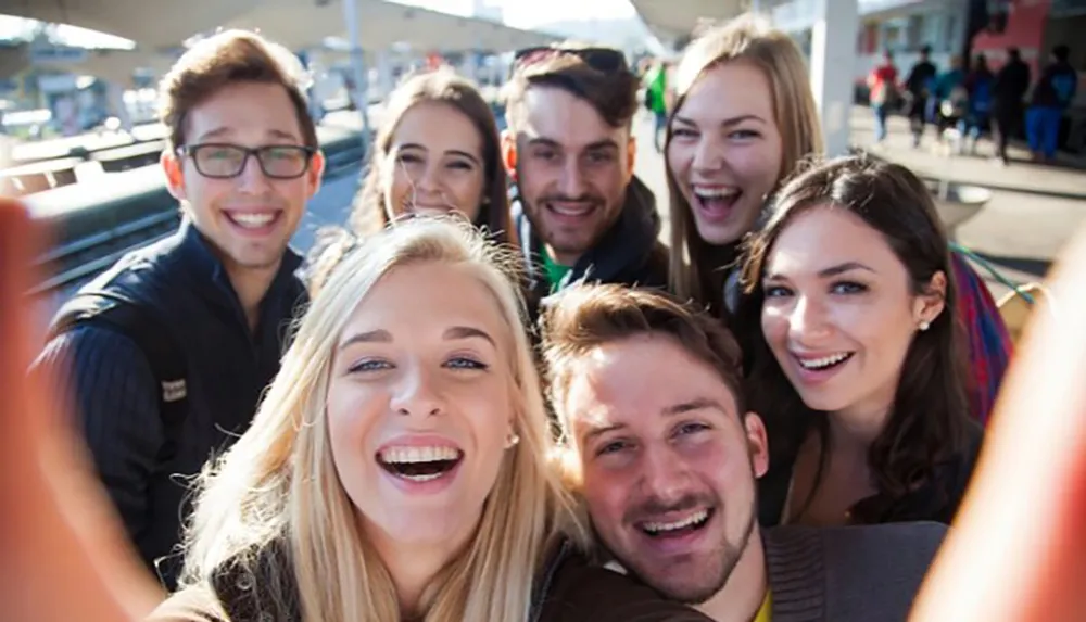 A group of cheerful young adults is taking a selfie with one of them holding the camera out in front capturing their smiling faces