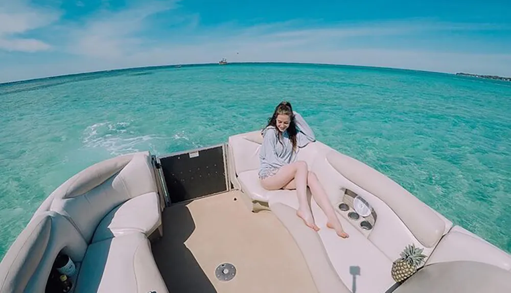 A person is sitting on the bow of a boat enjoying the clear turquoise waters of a sunny coastal environment