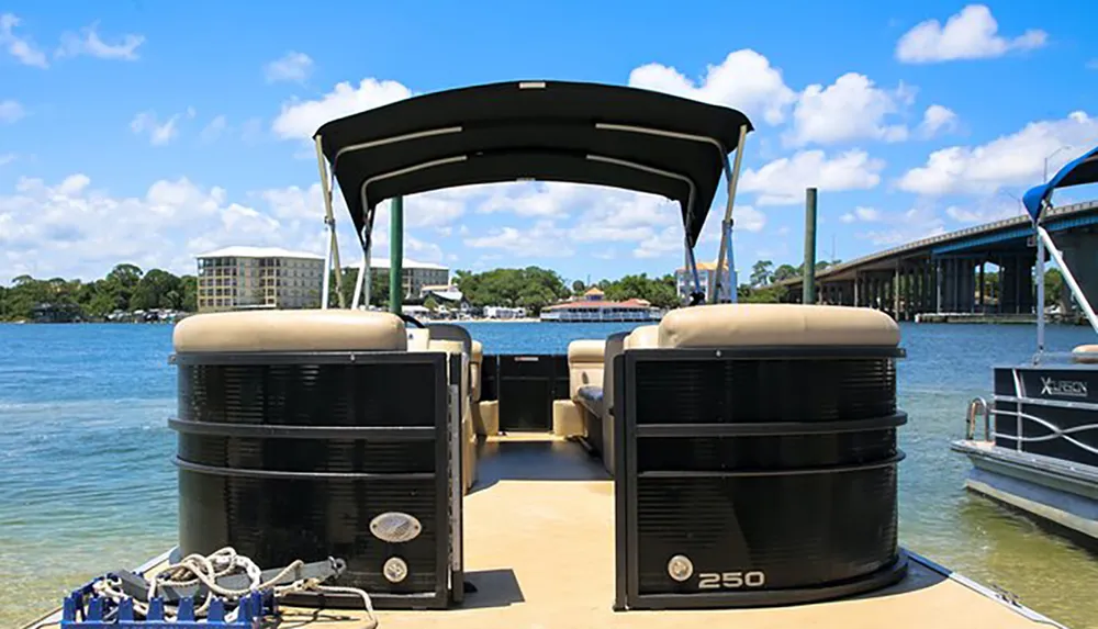 The image shows the interior of a pontoon boat docked in a sunny waterfront setting with buildings and a bridge in the background