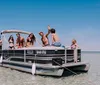 A group of young people are enjoying a sunny day on a pontoon boat waving and smiling with clear blue skies and water in the background